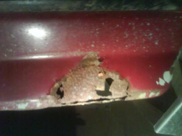 Close-up of red metal panel with significant rust damage and holes