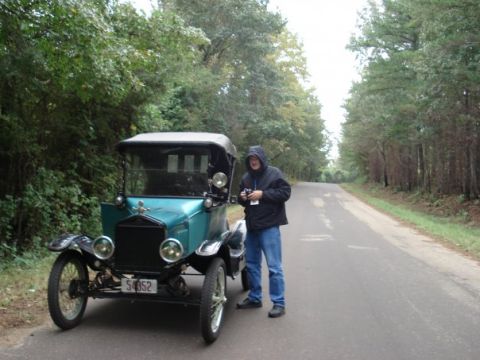 1917 Ford Model T - A person stands beside a teal 1917 Ford Model T on a paved road surrounded by trees.