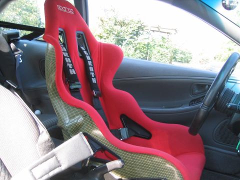 1993 Ford Probe - Interior view of a red racing seat with harnesses, likely a Sparco seat and Schroth harnesses.