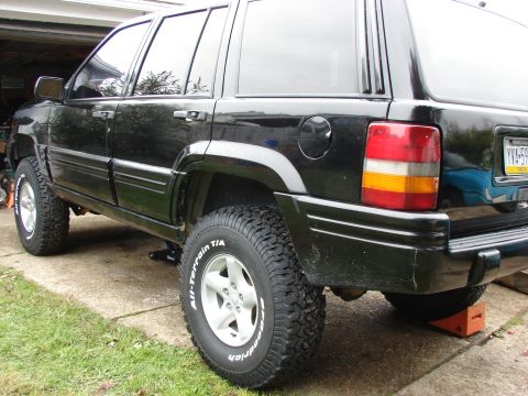 1996 Jeep Grand Cherokee - A black 1996 Jeep Grand Cherokee is shown from the rear quarter angle, lifted and equipped with off-road tires.