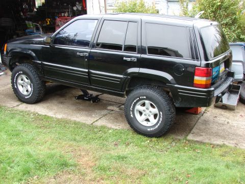 1996 Jeep Grand Cherokee - A black 1996 Jeep Grand Cherokee is shown from the side, supported by a jack.