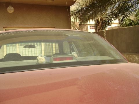 1998 Ford Crown Victoria - The rear of a red car is visible, showing a dusty window with interior items.