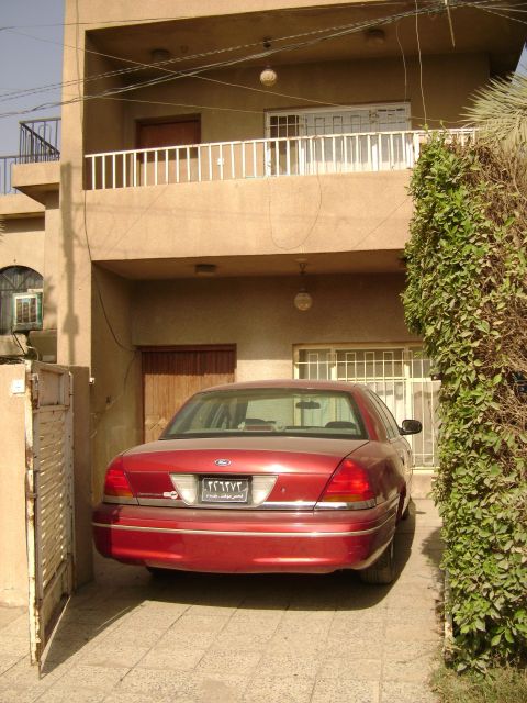 1998 Ford Crown Victoria - A red sedan is parked in a driveway in front of a multi-story building.