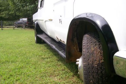 1982 Ford E350 - A white truck with visible rust and black fender flares is parked on grass next to another vehicle.