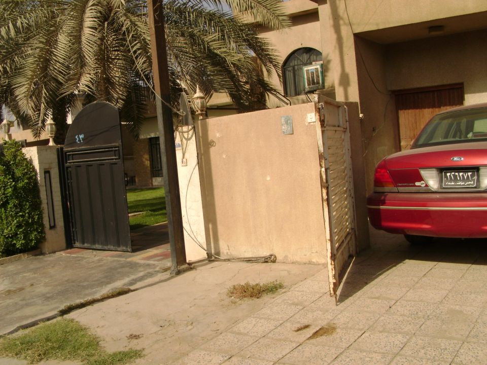 Red sedan parked in driveway, rear view. Visible taillights and license plate