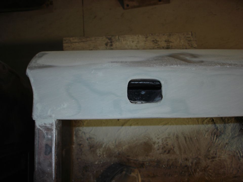 Part of a vehicle door with a square hole, covered in primer