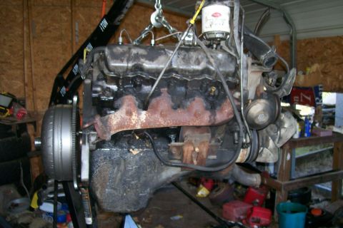 1992 Ford C-350 (Centurion Conversions) - Engine and transmission assembly suspended by an engine hoist in a garage setting.