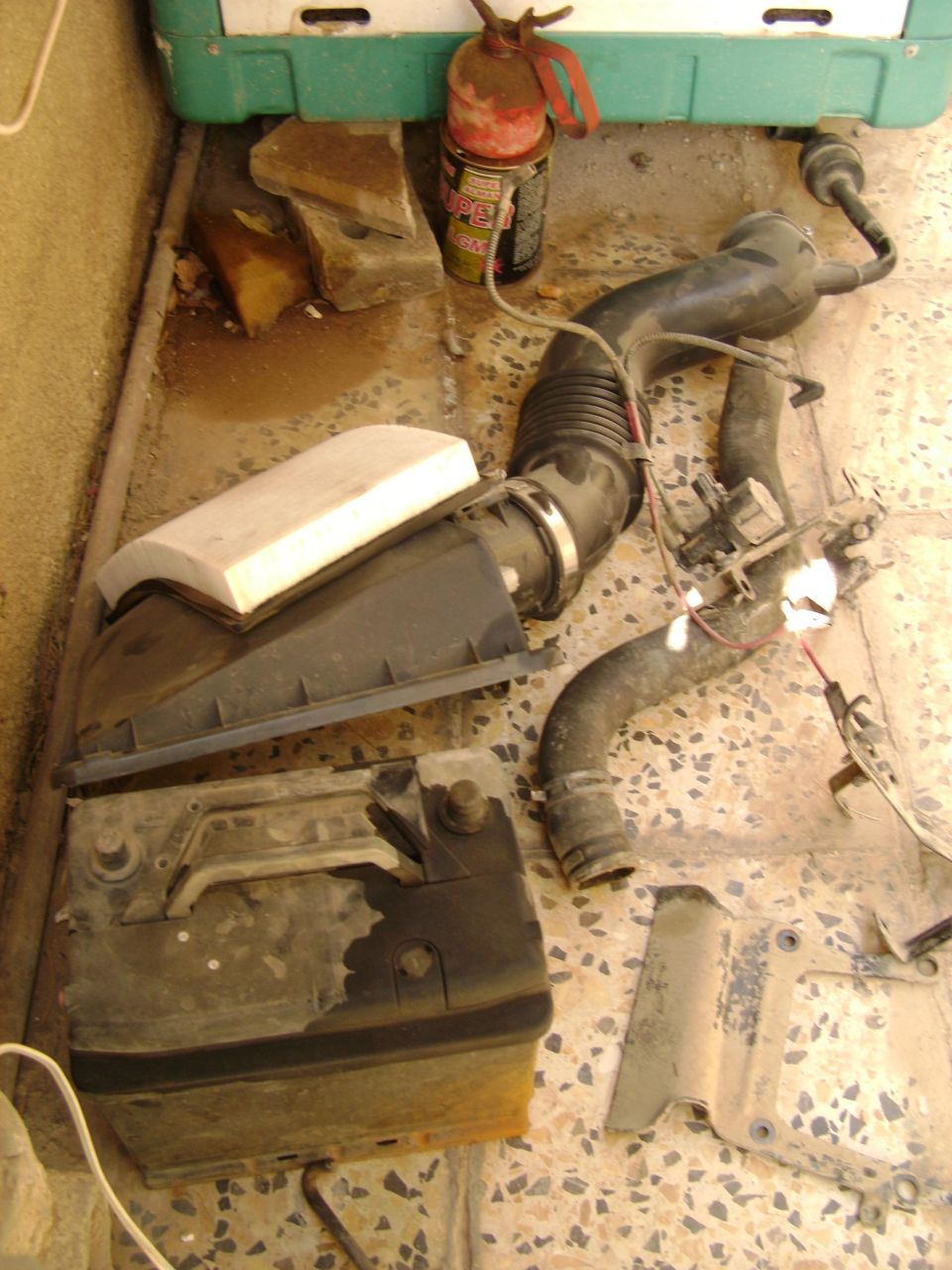 Disassembled car parts: air intake assembly, battery, and hoses on a tiled floor