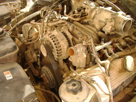 1998 Ford Crown Victoria - The engine bay of a 1998 Ford Crown Victoria shows significant dust and grime, with the alternator and intake manifold prominently visible.