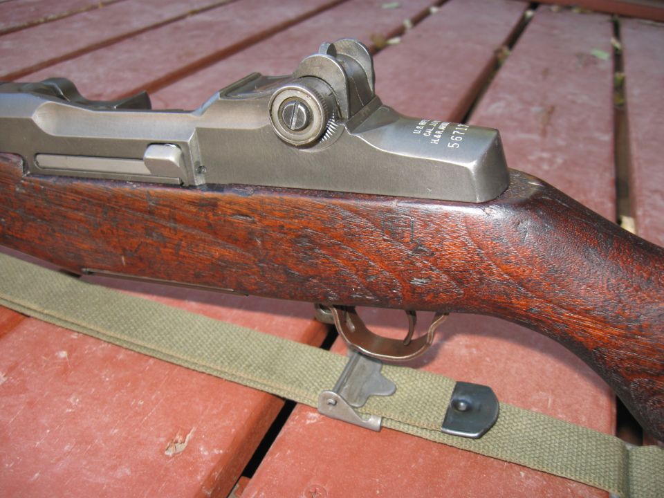 M1 Garand rifle with wooden stock and metal receiver, green sling, on red wooden surface