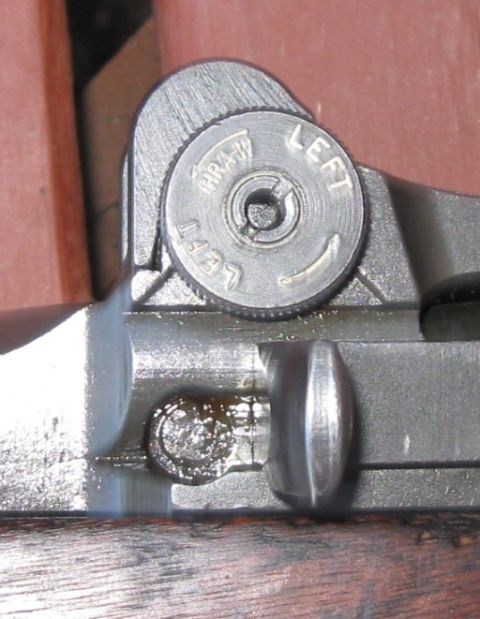 2000 Ford Crown Victoria - This close-up shows the adjustment knob on a firearm's rear sight, with directional and manufacturer markings visible.