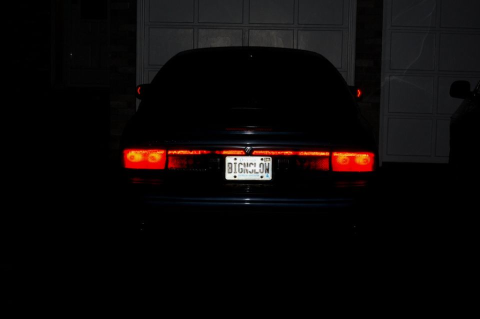 Rear of dark sedan at night with glowing red taillights and 'BIGNSLOW' plate