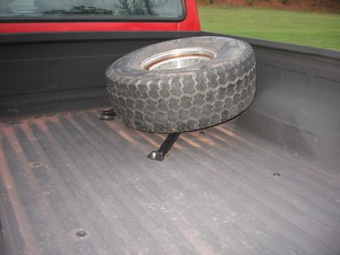 1995 Ford F-150 - A spare tire is secured in the bed of a red truck, with the truck bed floor visible.