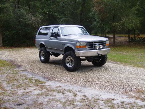 1995 Ford Bronco - This lifted Ford Bronco is parked on a gravel surface with trees in the background.