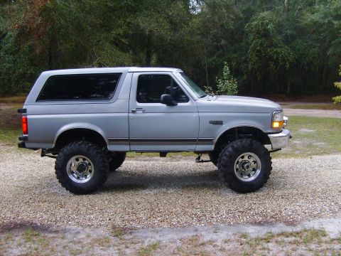1995 Ford Bronco - This lifted 1995 Ford Bronco is shown in a side profile view on a gravel surface with trees in the background.