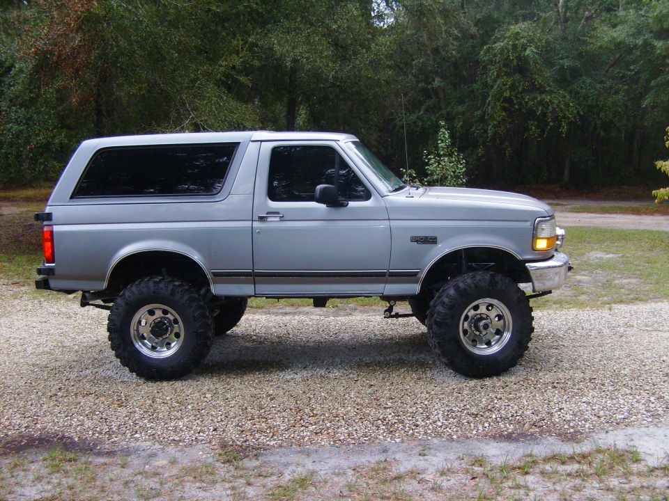 Lifted silver Ford Bronco side profile on gravel drive with mud tires and polished wheels