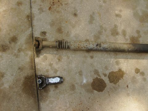 1995 Ford Bronco - A rusty driveshaft and a metal U-joint lie on a concrete surface.