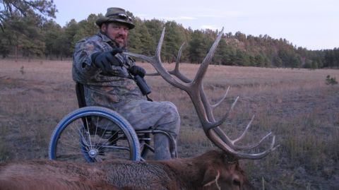 1983 Jeep CJ7 - Hunter poses with his elk kill, seated in a wheelchair in a field with trees in the background.
