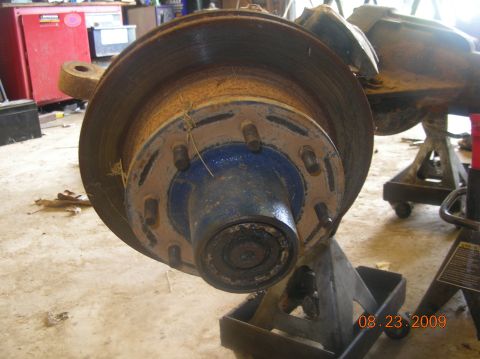 1991 Ford F-150 - A close-up of a rusty truck wheel hub and brake rotor assembly, resting on jack stands in a workshop.