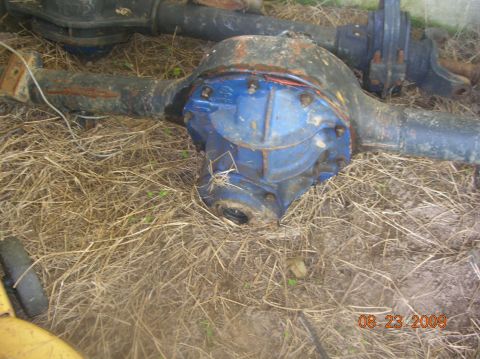 1991 Ford F-150 - A rear axle assembly with a blue differential housing sits on dry grass, with another axle visible behind it.