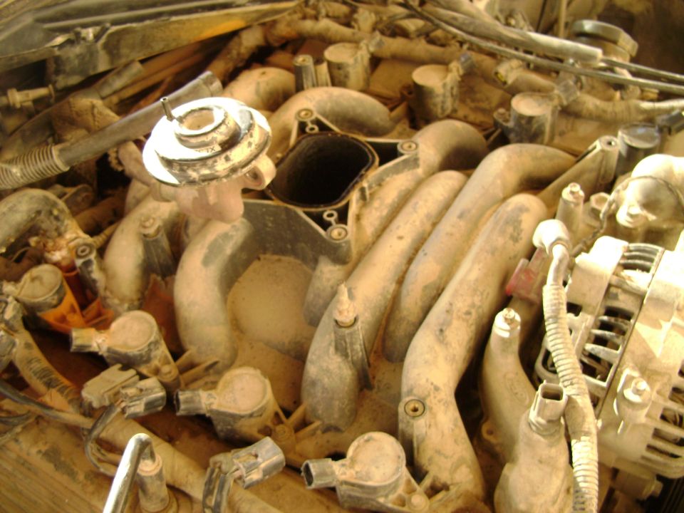 Close-up of a dirty engine intake manifold with hoses and an alternator visible