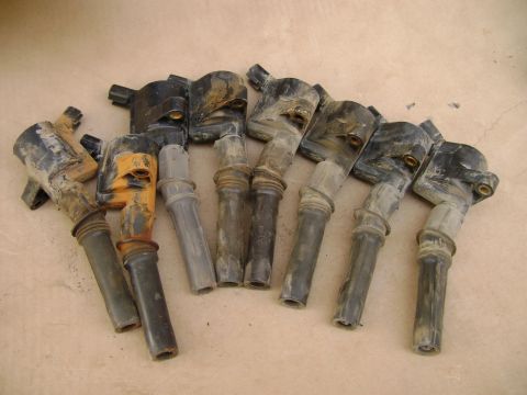 1998 Ford Crown Victoria - A collection of used ignition coils are shown, some with orange accents, lying on a textured surface.