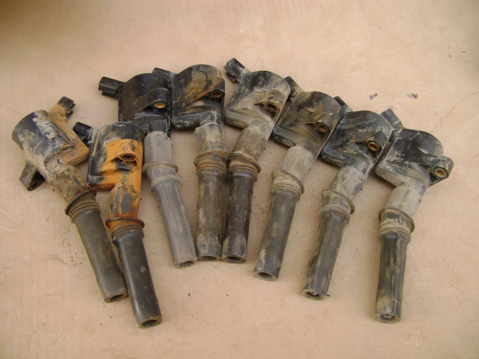 Several dirty ignition coils scattered on a light brown surface