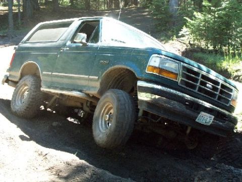1982 Ford Bronco - This green Ford Bronco is navigating a steep, muddy incline in a wooded area.