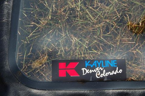 1994 Ford Bronco - A sticker for Kayline Denver Colorado is visible on the window of a vehicle, with grass seen through the glass.