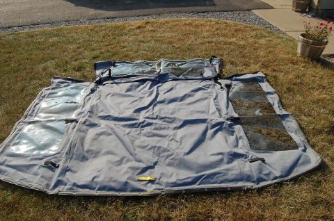 1994 Ford Bronco - A gray fabric soft top with multiple clear plastic windows is spread out on a grassy lawn.