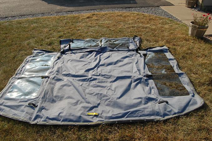 Gray fabric soft top with clear plastic windows laid out on grass