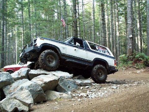 1982 Ford Bronco - A 1982 Ford Bronco navigates a rocky trail in a wooded area, with another vehicle visible in the background.