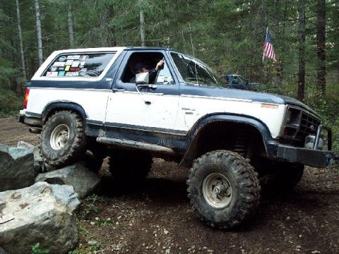 1982 Ford Bronco - 1982 Ford Bronco navigating a rocky off-road course in a wooded area.