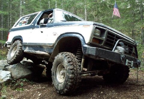 1982 Ford Bronco - This modified SUV is navigating a challenging rocky terrain on a wooded trail.