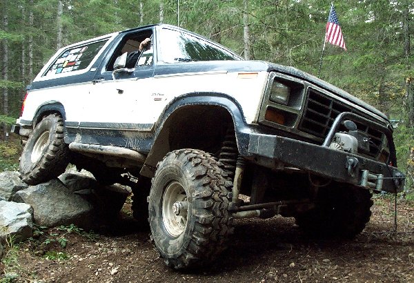 Lifted white and blue Ford Bronco flexing over rocks with winch and American flag