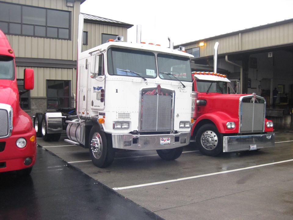 1981 Kenworth W900A and a red semi-truck parked in front of a building