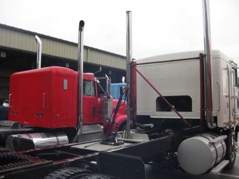 1981 Kenworth W900A - Two semi-truck cabs are parked next to each other, with a blue truck visible behind the red one.