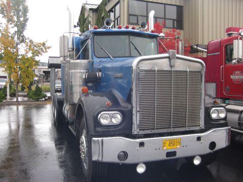1981 Kenworth W900A - A blue 1981 Kenworth W900A truck is parked next to a red fire truck on a rainy day.