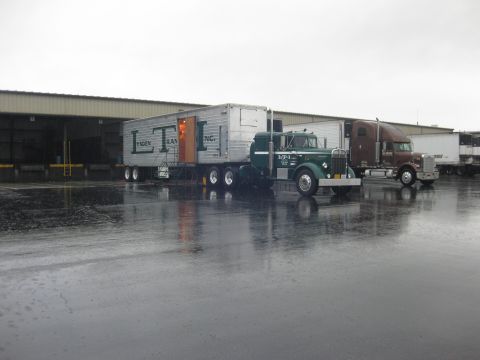 1981 Kenworth W900A - A green vintage semi-truck is parked next to a loading dock with a trailer, while another truck is visible in the background.