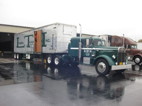 1981 Kenworth W900A - A classic green Kenworth semi-truck and trailer are parked on a wet surface near a warehouse loading dock.