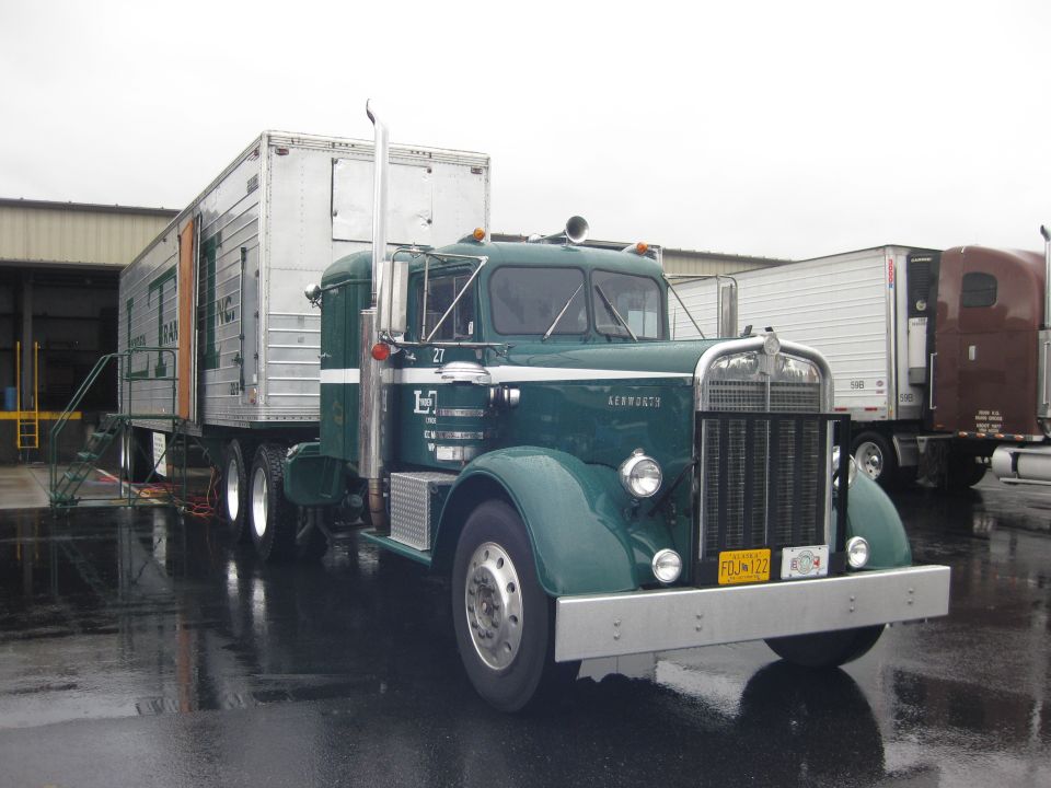 Green 1970s Kenworth truck with a silver trailer, parked on wet asphalt