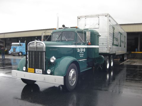 1981 Kenworth W900A - A green Kenworth semi-truck is parked next to a loading dock, with another blue truck visible in the background.