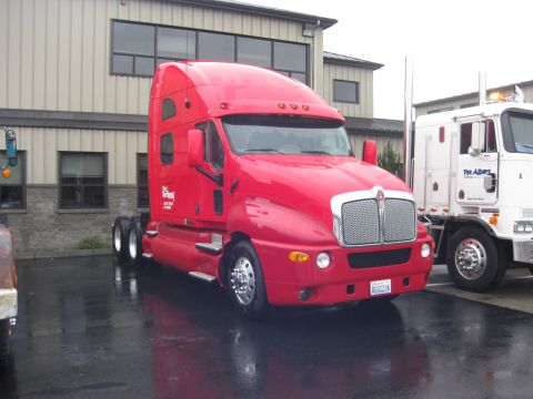 1981 Kenworth W900A - A red semi-truck is parked next to a white truck in front of a building.