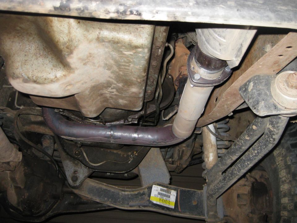 Truck underbody with transmission pan, exhaust crossover pipe and coil spring