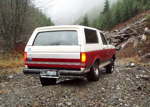 1982 Ford Bronco - A two-tone red and white 1982 Ford Bronco is seen from the rear on a rocky, wooded trail.