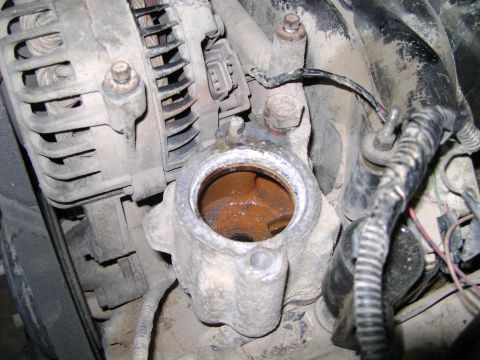 1998 Ford Crown Victoria - Close-up of a corroded engine part with visible wiring and a water-stained opening.