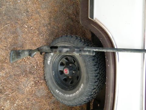1982 Ford Bronco - A camouflage shotgun lies across a tire, with part of a trailer visible in the background.