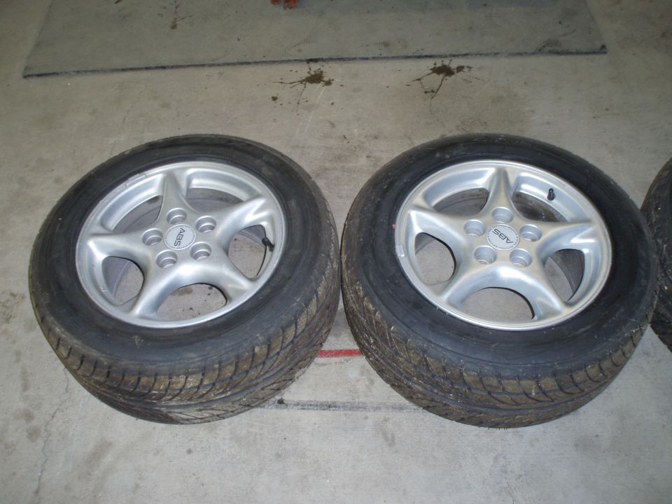 Two silver 5-spoke wheels with tires on a concrete floor. One wheel has an 'ABS' logo visible