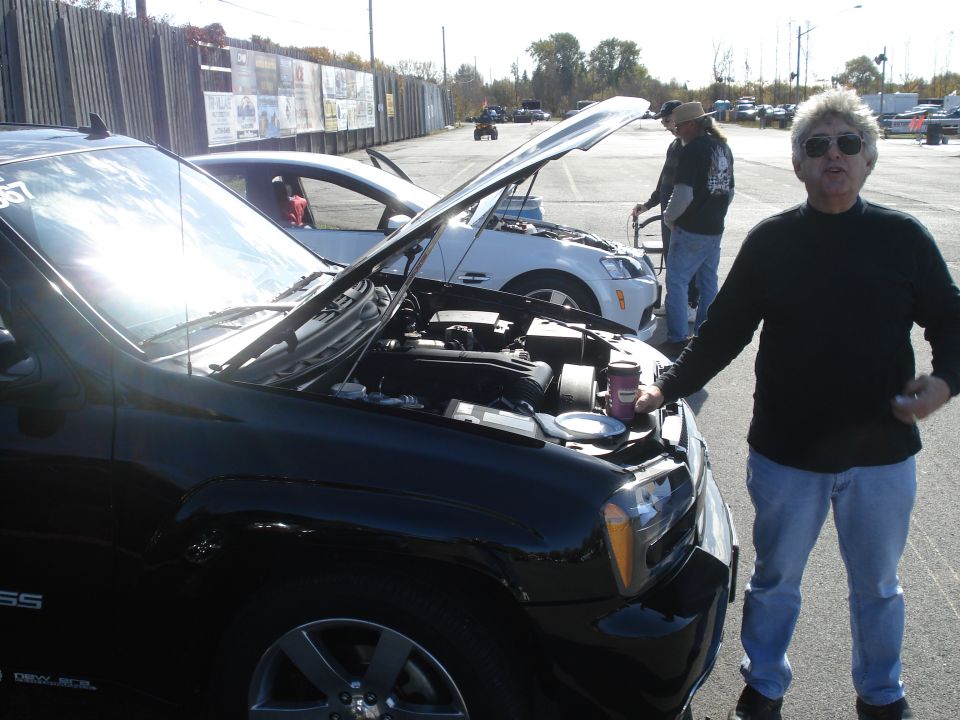 Black SUV and white sedan with hoods open at a drag strip, people standing nearby