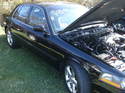 2000 Ford Crown Victoria - A black sedan is parked on grass with its hood open, revealing the engine compartment. The number 518 is written on the windshield.